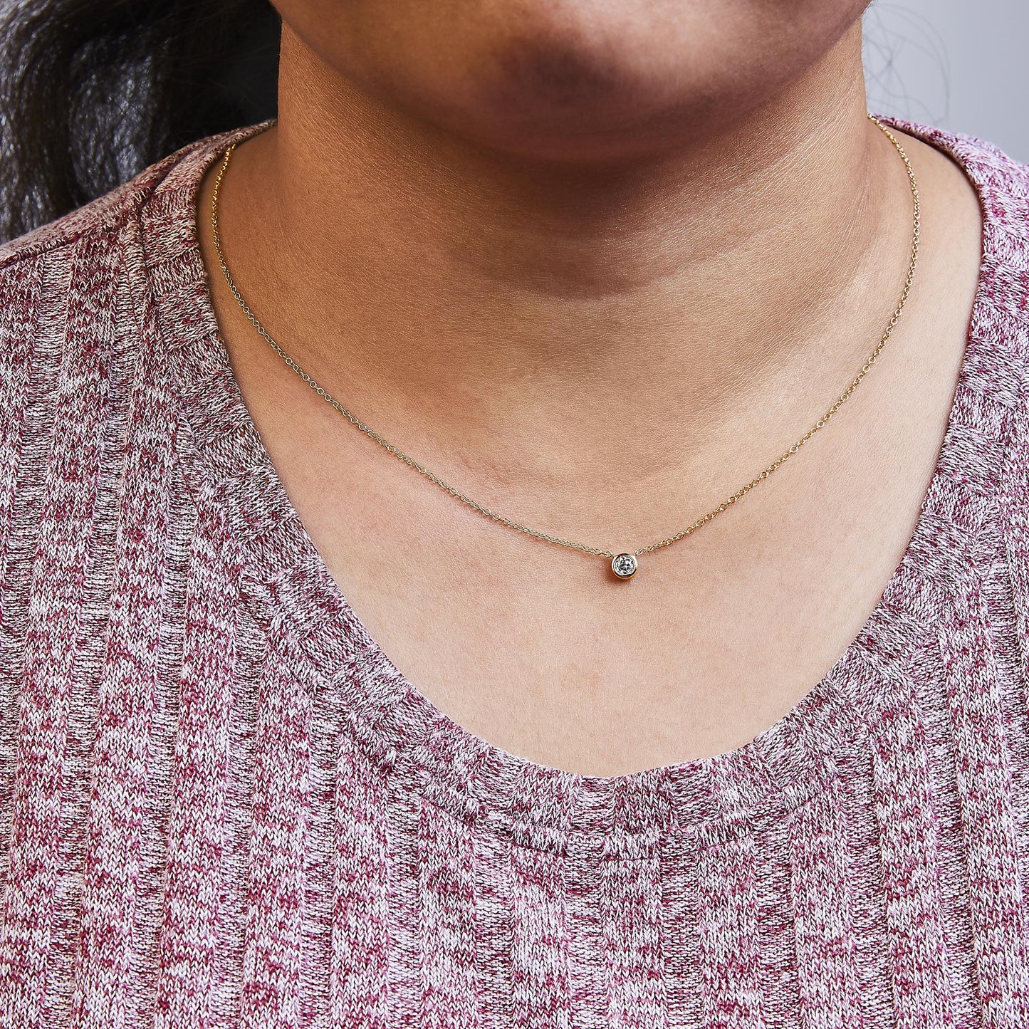 Close-up view of a yellow metal necklace with a round white gemstone in a bezel setting, worn on a model.