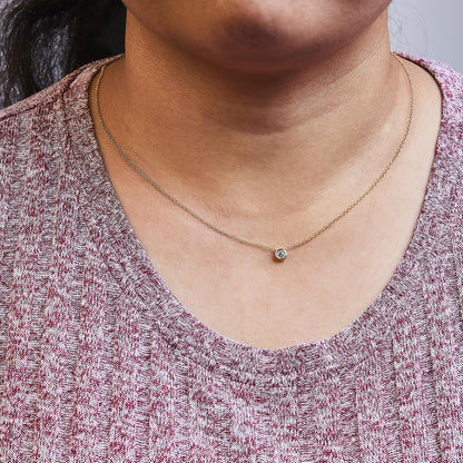 Close-up view of a yellow metal necklace with a round white gemstone in a bezel setting, worn on a model.