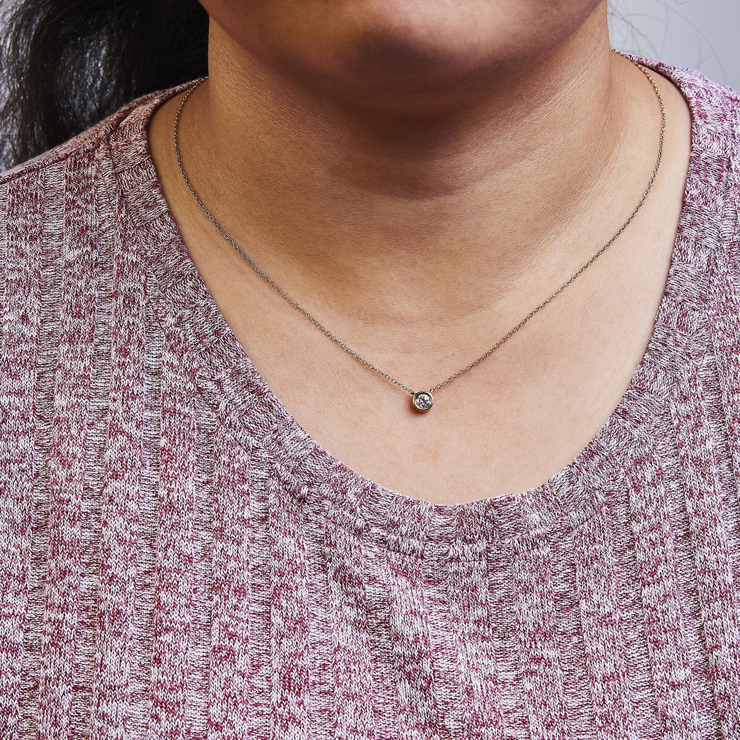 Close-up front view of a rose metal necklace with a round bezel-set white gemstone pendant worn on a model.