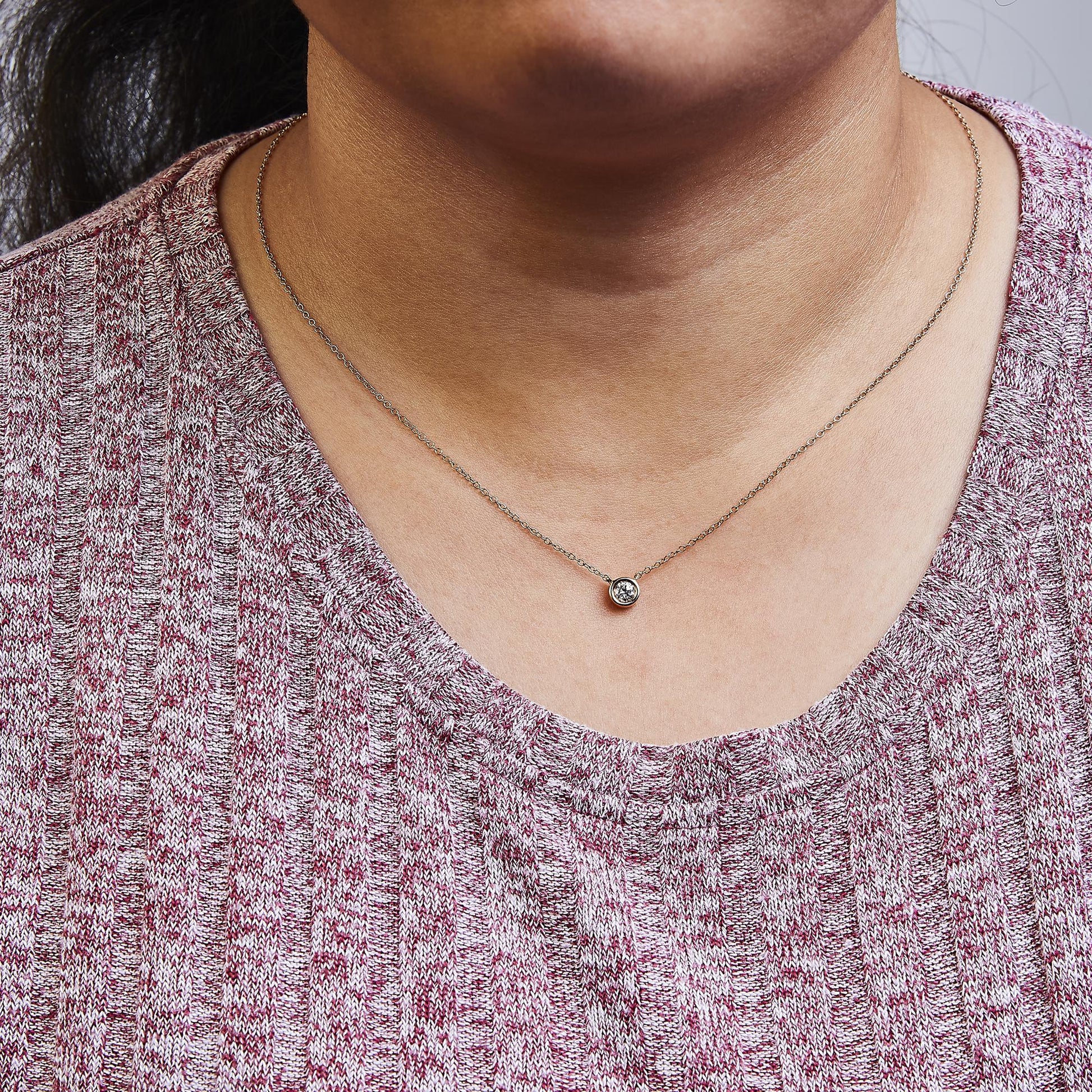 Close-up front view of a rose metal necklace with a round bezel-set white gemstone pendant worn on a model.