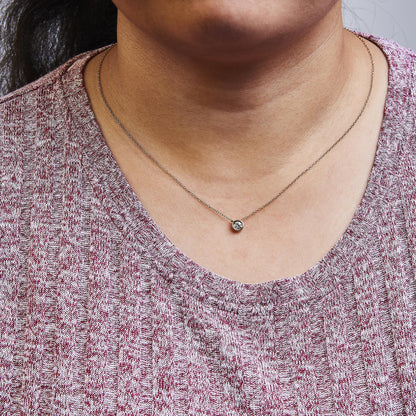 Close-up front view of a rose metal necklace with a round bezel-set white gemstone pendant worn on a model.