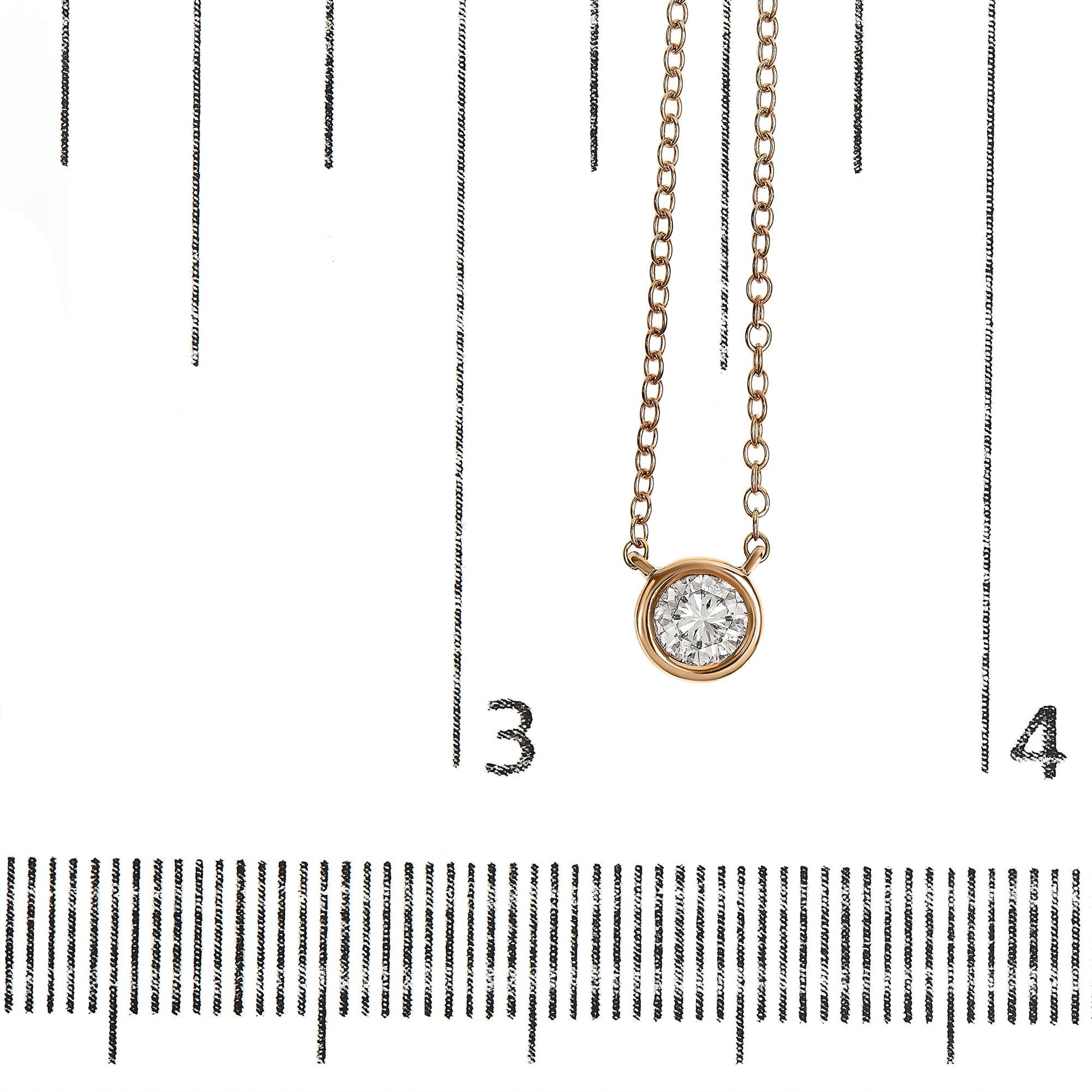 Rose-colored necklace with a round white gemstone in a bezel setting, photographed from the front on a ruler for size reference.