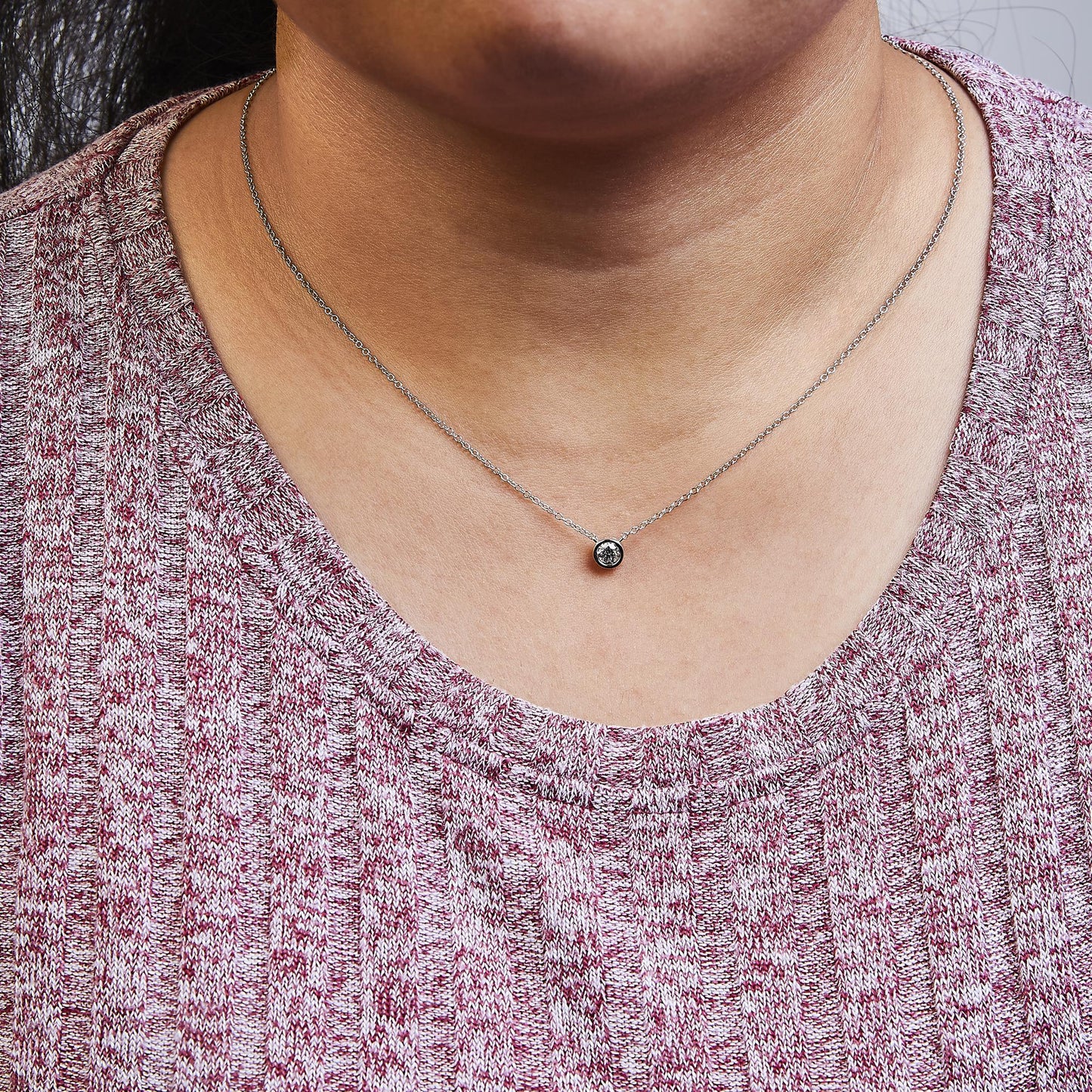 Close-up front view of a white metal necklace with a round white gemstone in a bezel setting, worn on a model.