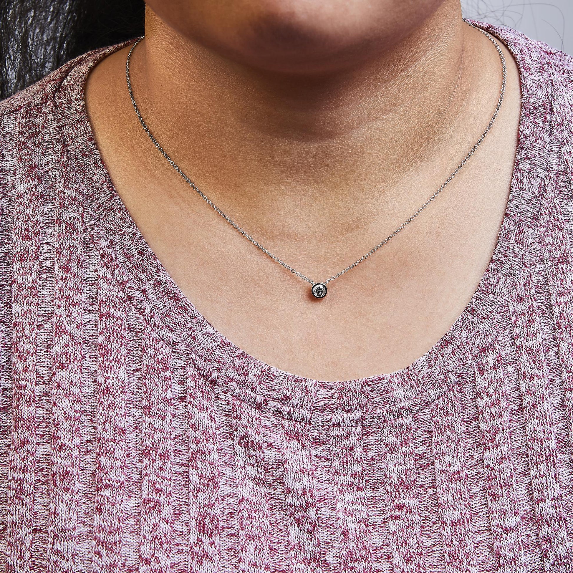 Close-up front view of a white metal necklace with a round white gemstone in a bezel setting, worn on a model.