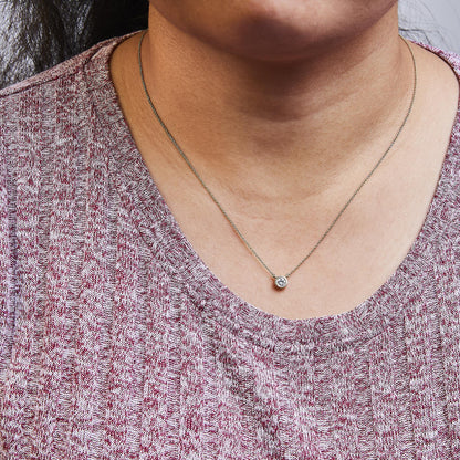 Close-up front view of a yellow metal necklace with a round bezel-set white gemstone pendant worn on a model.