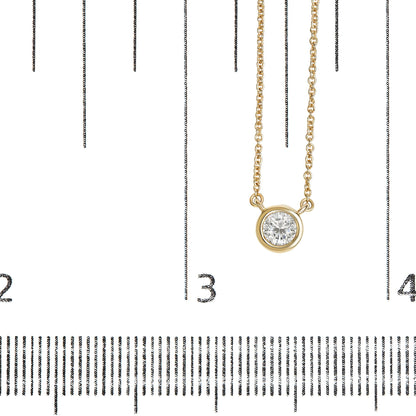 Close-up front view of a yellow metal necklace with a round white gemstone in bezel setting, displayed on a ruler for size reference.