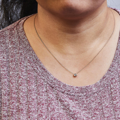 Close-up front view of a rose metal necklace on a model, featuring a round white gemstone in a bezel setting pendant.