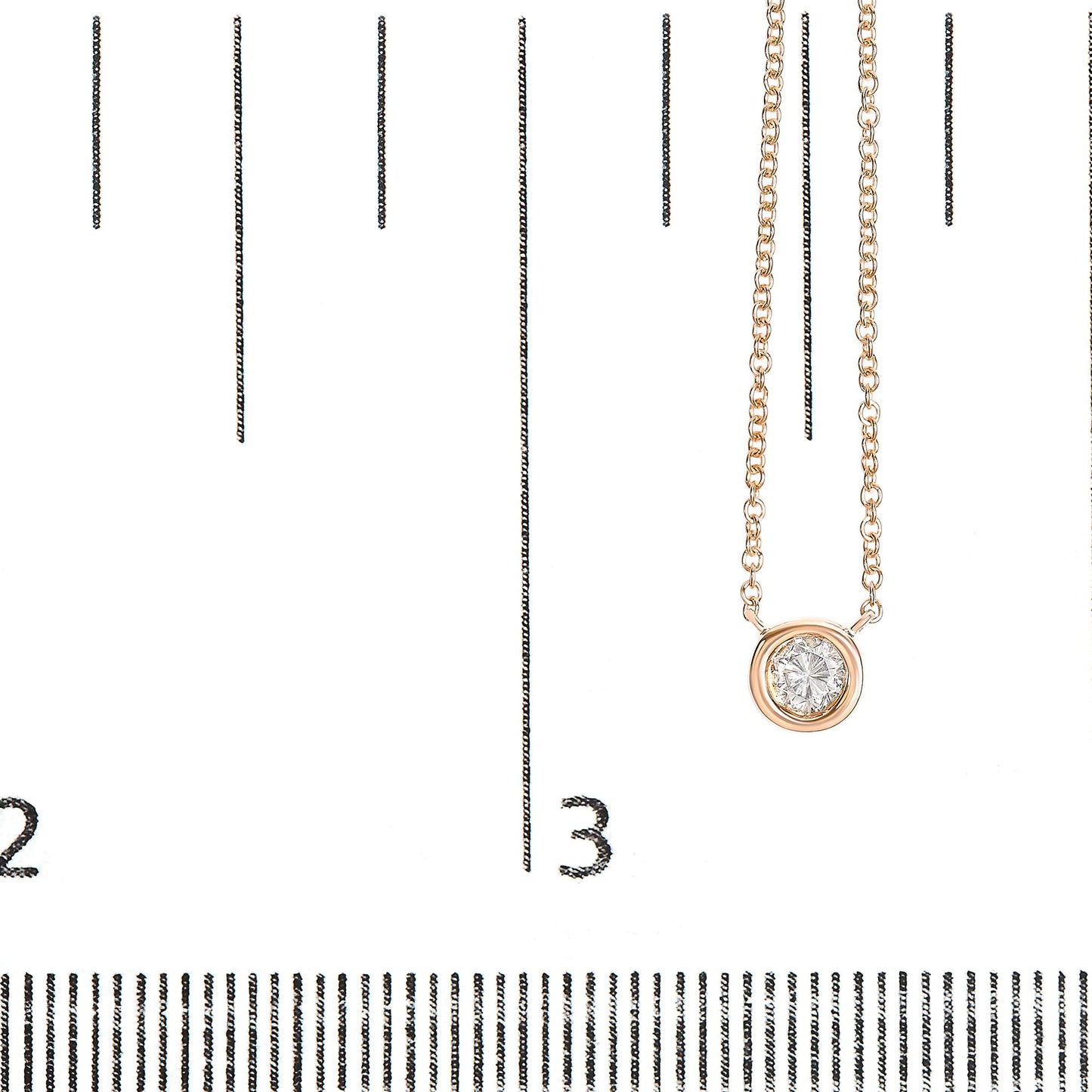 Close-up front angle of a rose metal necklace with a round white gemstone in bezel setting, displayed on a ruler for size reference.