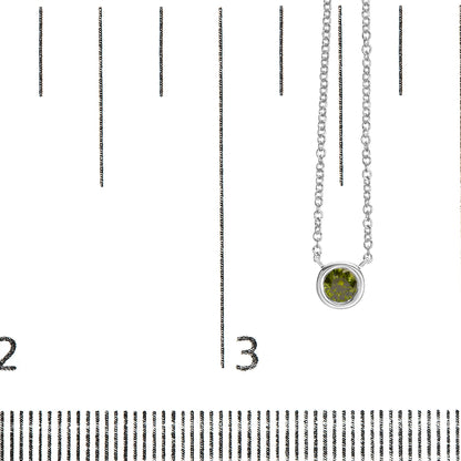 Close-up front view of a white metal necklace with a round green gemstone in a bezel setting, displayed on a ruler for size reference.