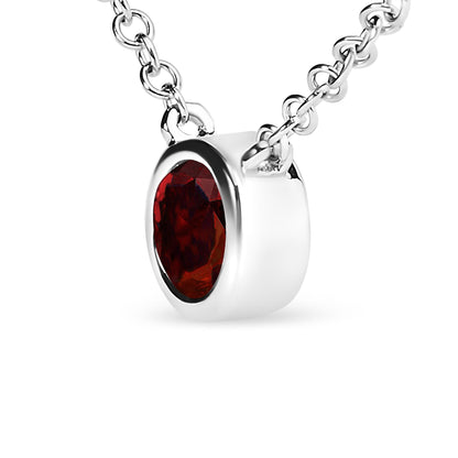 Close-up angled view of a white metal necklace with a round red gemstone in a bezel setting.