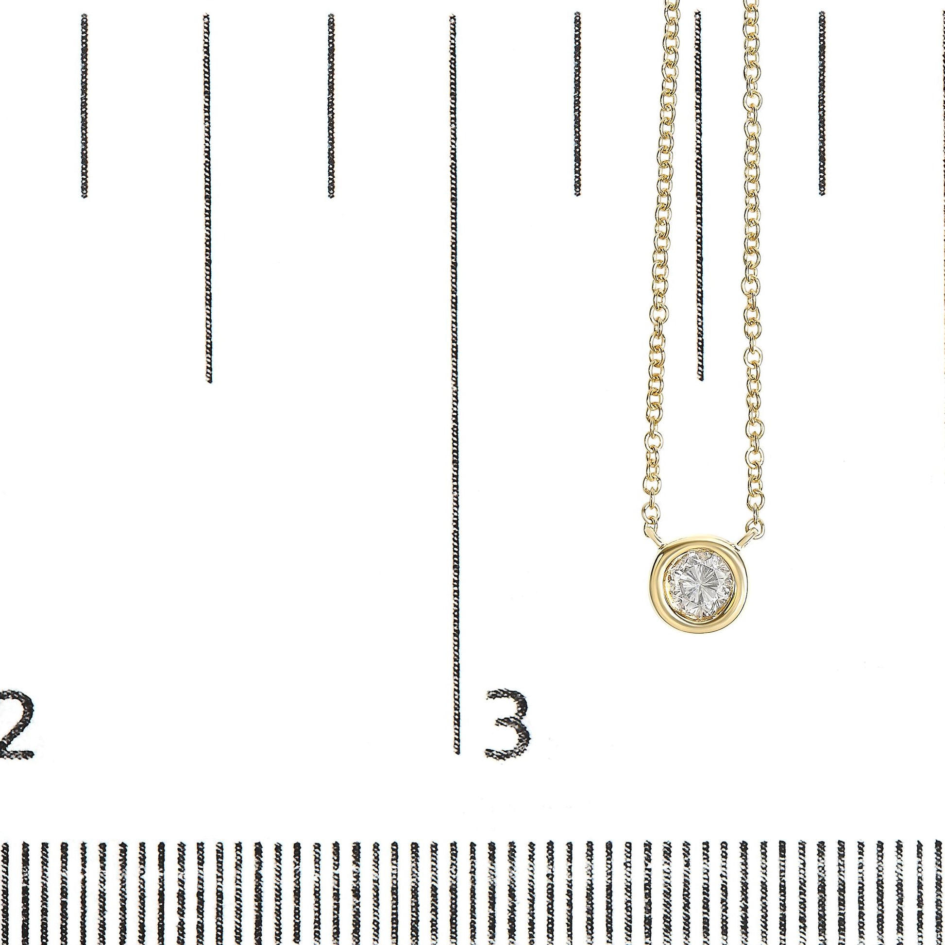 Close-up front angle of a yellow metal necklace with a round white gemstone in bezel setting, displayed on a ruler for size reference.