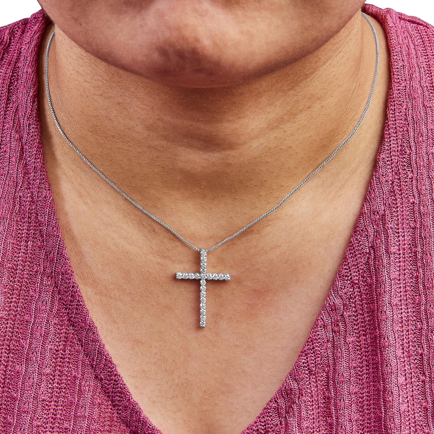Close-up front view of a white metal necklace with a cross-shaped pendant featuring round white gemstones in prong settings, worn on a model.