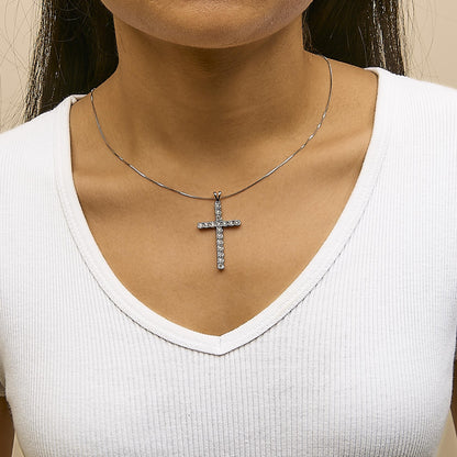 Close-up front view of a model wearing a white metal necklace with a cross pendant set with multiple round white gemstones.