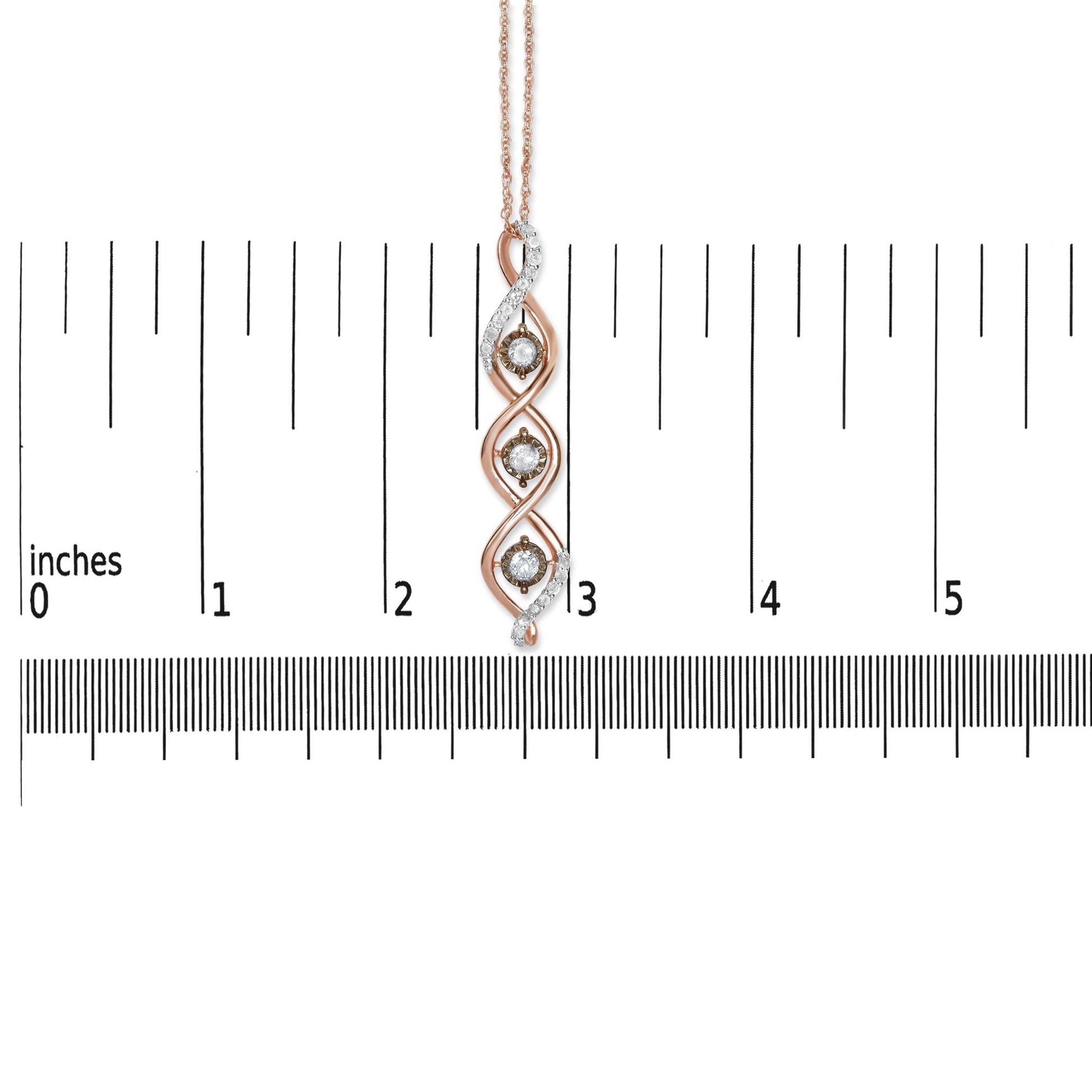 Close-up image of a two-toned necklace pendant with three round white gemstones in prong settings and three round champagne-colored gemstones in miracle settings, displayed vertically on a ruler for size reference.