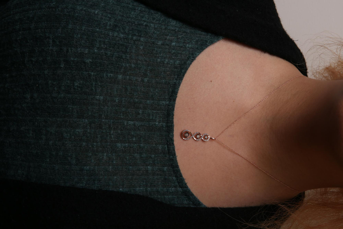 Close-up front view of a two-toned necklace on a model, featuring a vertical pendant with intertwined loops set with white gemstones and three champagne-colored gemstones in a miracle setting.