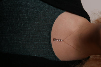 Close-up front view of a two-toned necklace on a model, featuring a vertical pendant with intertwined loops set with white gemstones and three champagne-colored gemstones in a miracle setting.
