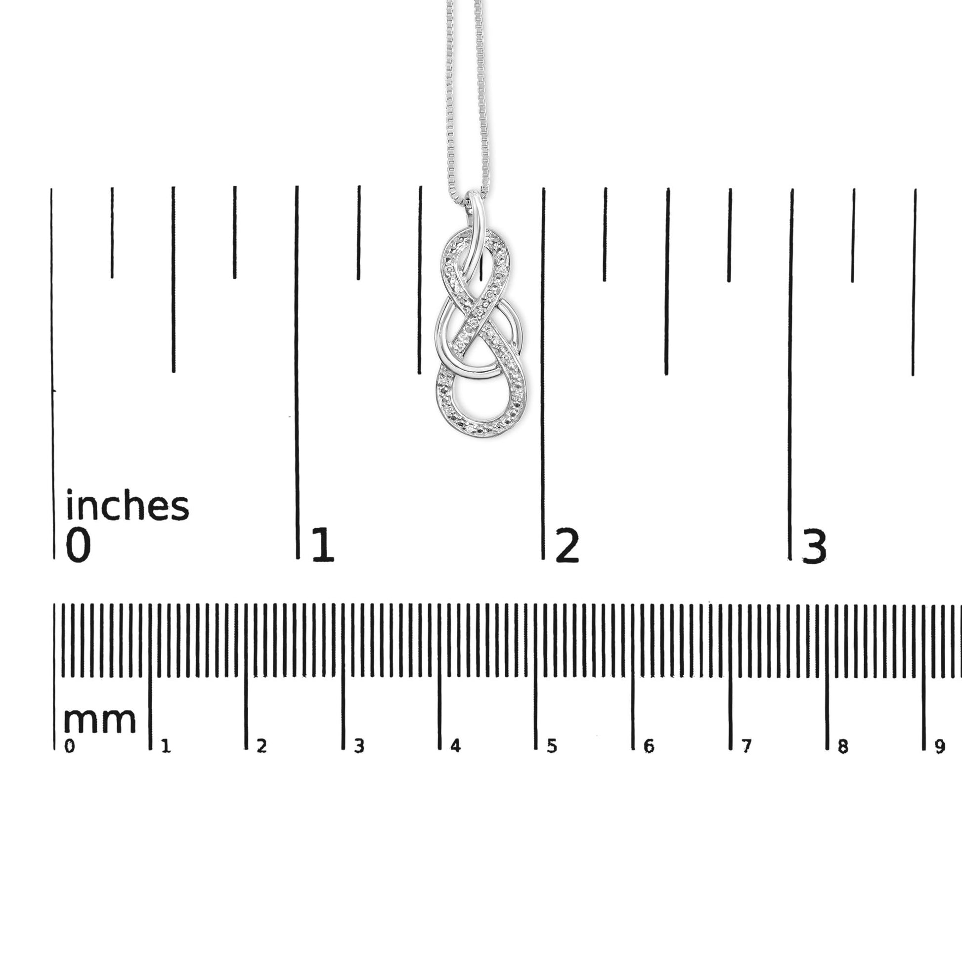 White metal necklace with an intertwined infinity pendant accented with round white gemstones, shown hanging against a ruler for size reference, front-facing angle.