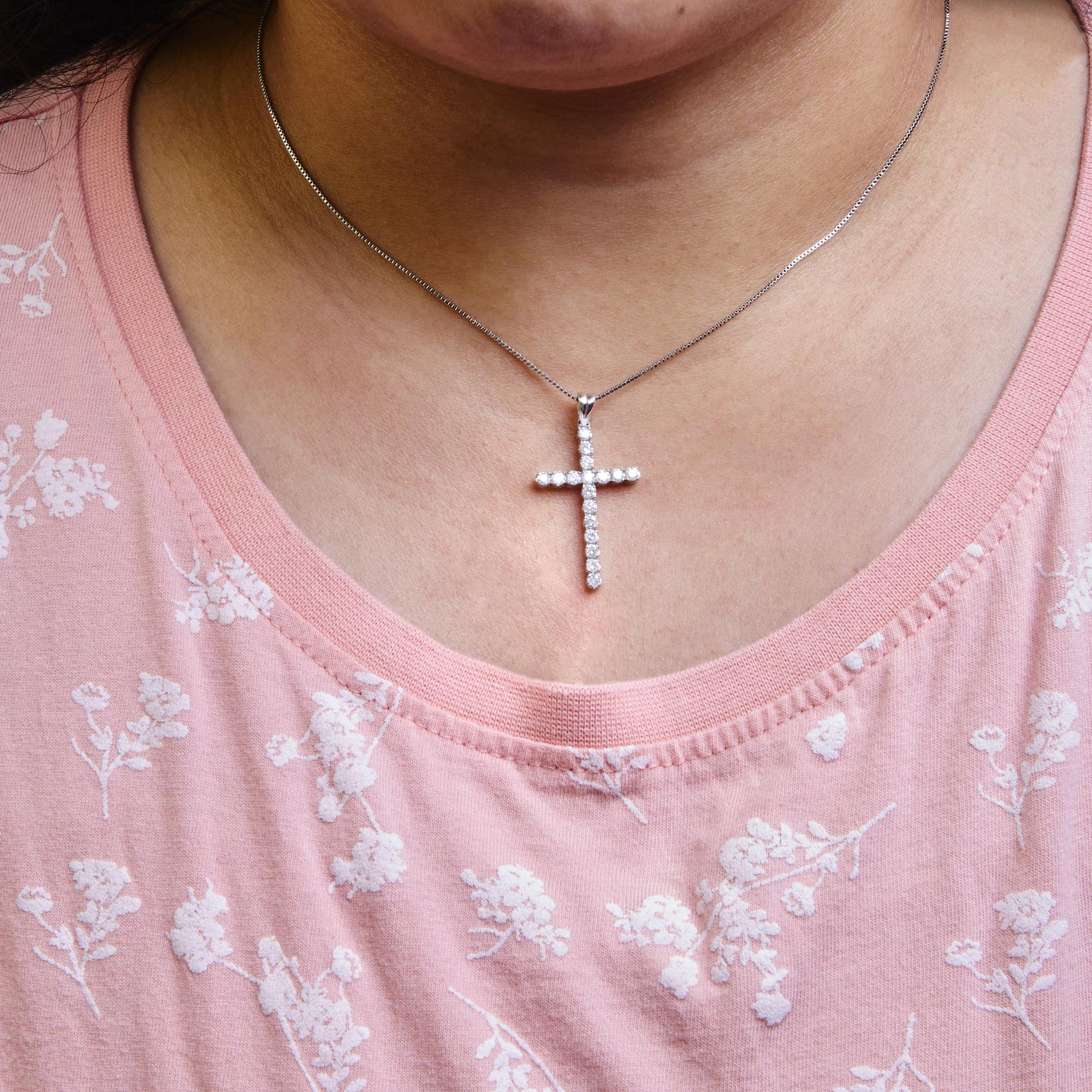 White metal necklace with cross pendant featuring round white gemstones in prong setting, worn on a model, front view.