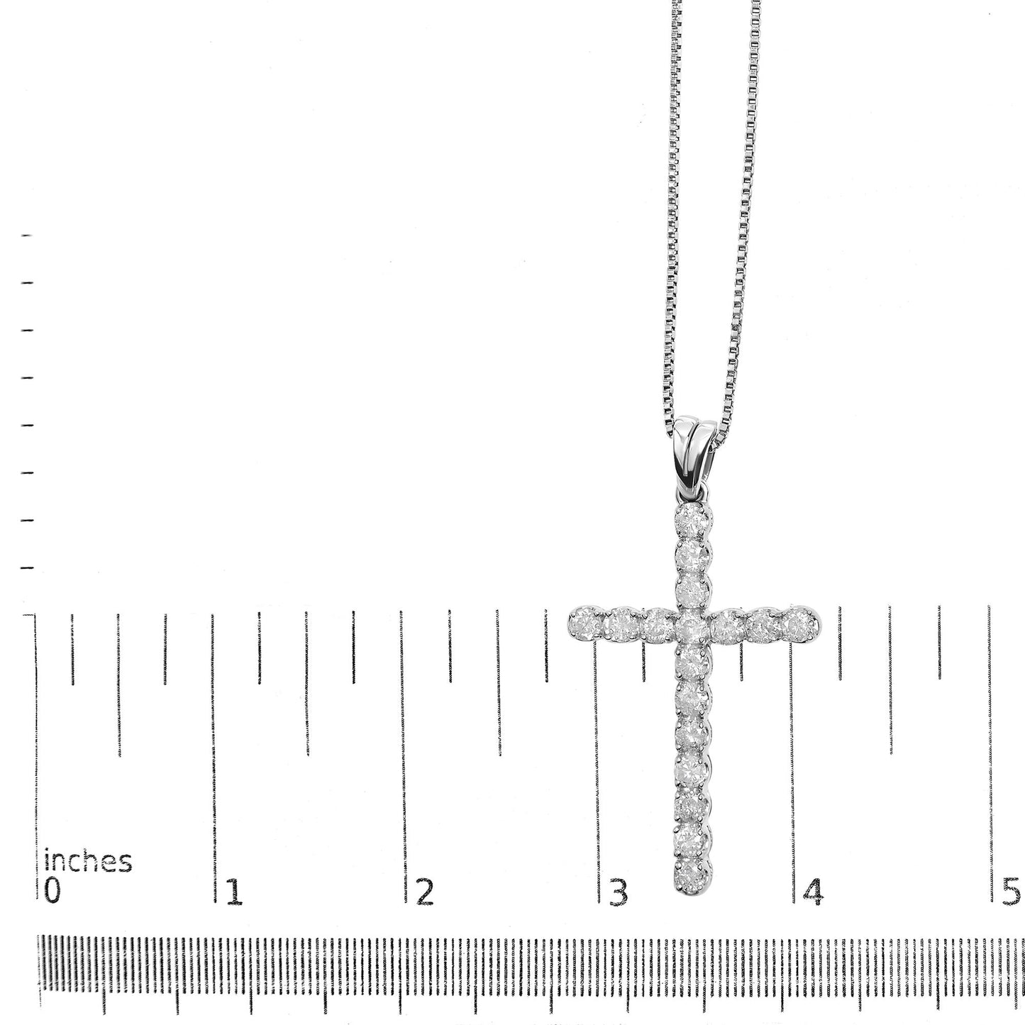 White metal necklace with a cross pendant featuring round white gemstones in prong settings, positioned flat on a ruler for size reference, shot from above.