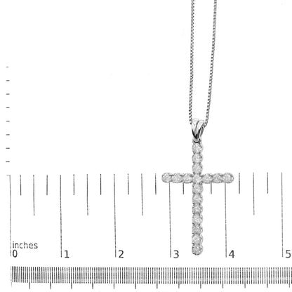 White metal necklace with a cross pendant featuring round white gemstones in prong settings, positioned flat on a ruler for size reference, shot from above.