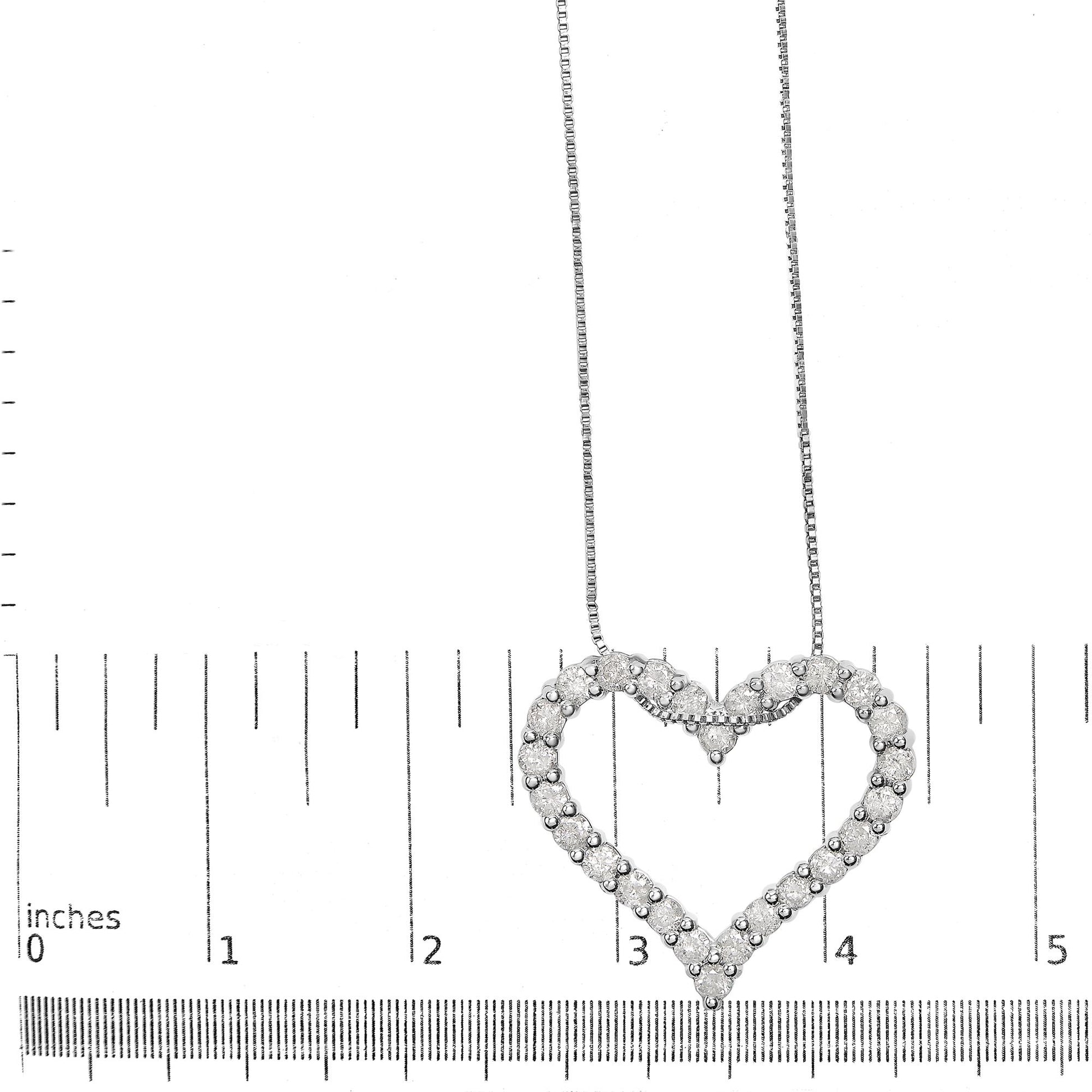 Top view of a white metal heart-shaped necklace pendant with round white gemstones in shared prong setting, displayed on a ruler for size reference.
