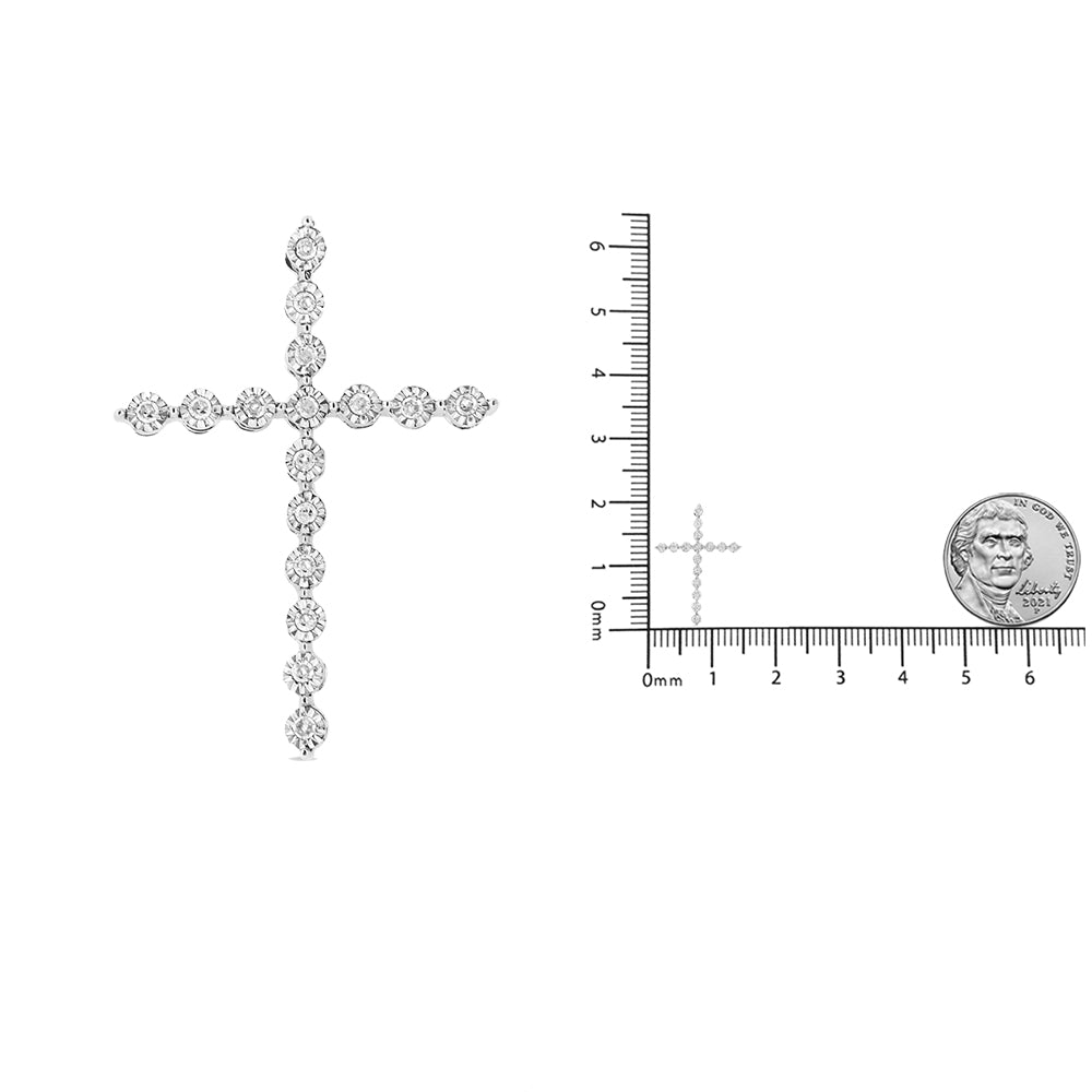 White metal cross-shaped necklace pendant with round white gemstones in miracle setting, shown from front on a ruler and coin for size reference.