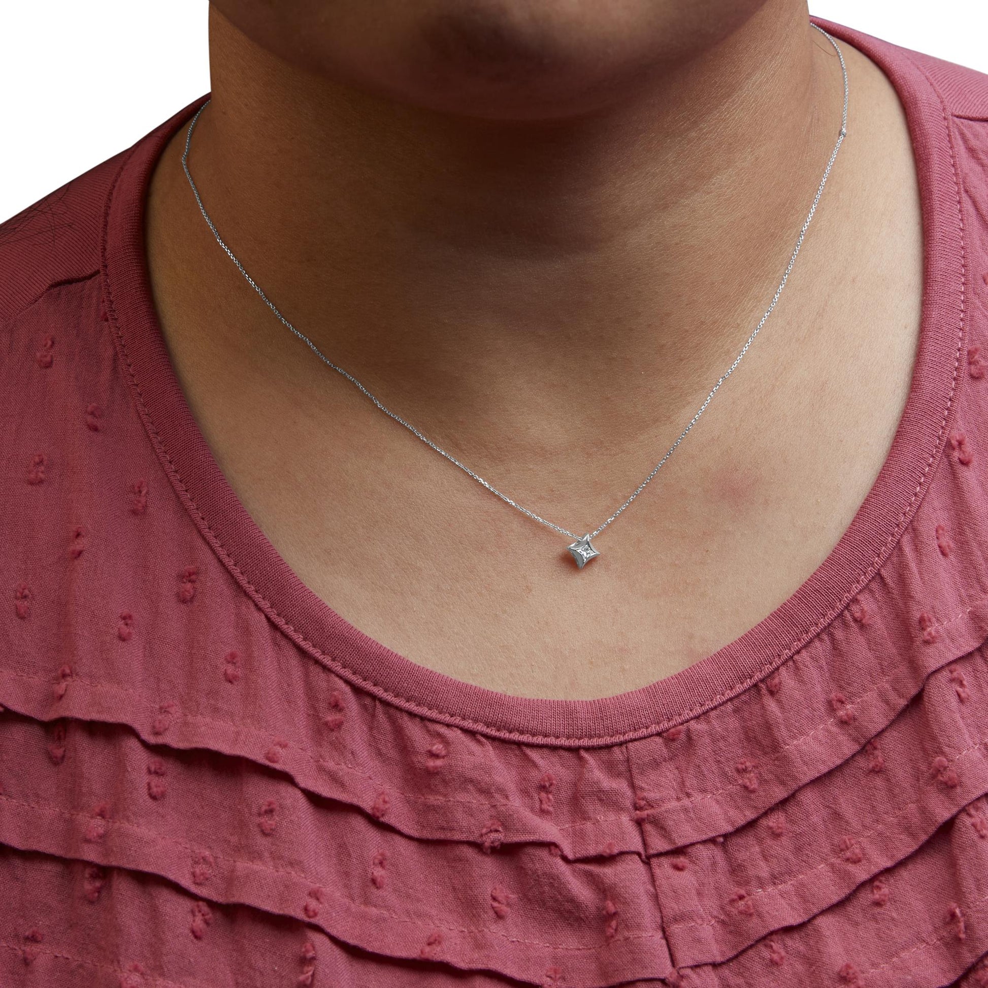 Close-up front view of a white metal necklace with a single princess-shaped pendant featuring one white gemstone, worn on a model wearing a textured red top.