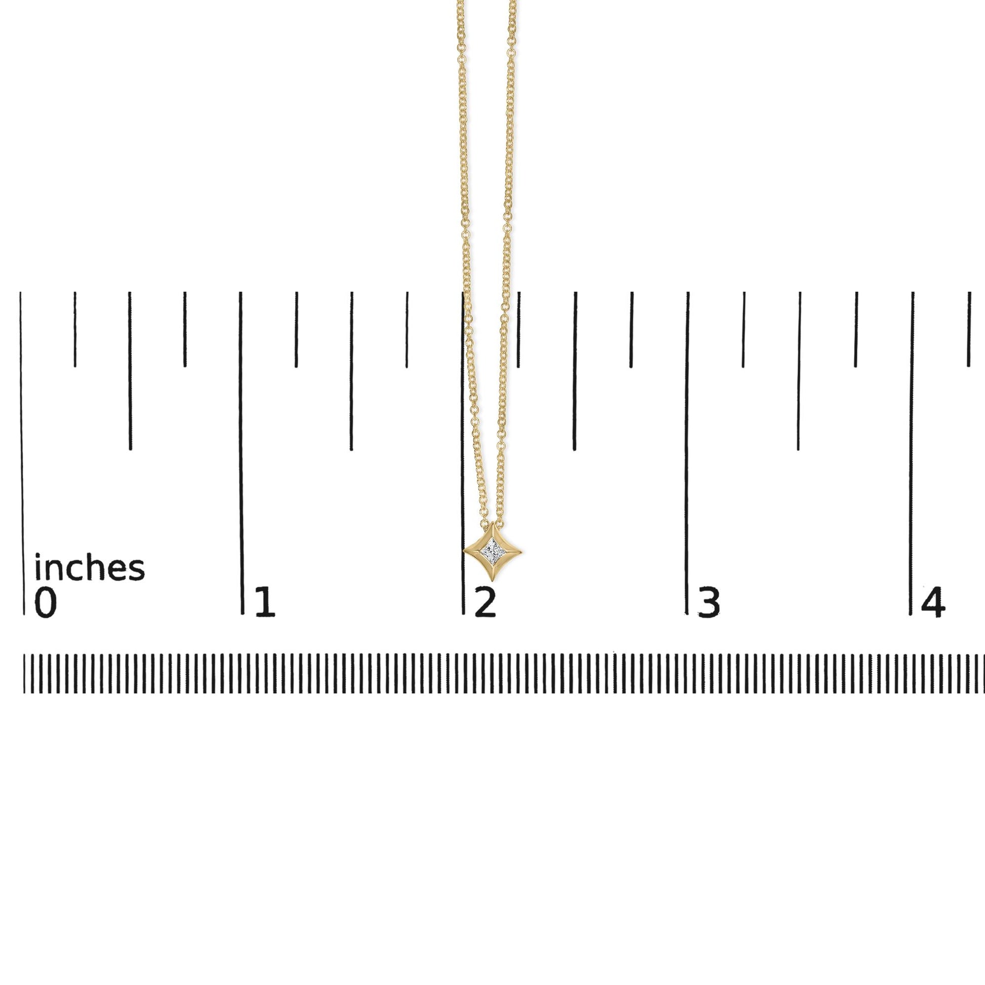 Front-facing shot of a yellow metal necklace with a princess-shaped white gemstone pendant, displayed on a ruler for size reference.