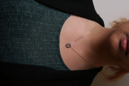 Close-up front view of a necklace with a yellow metal oval pendant featuring round blue and yellow gemstones in prong settings, worn on a model.