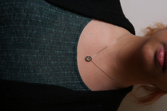 Close-up front view of a necklace with a yellow metal oval pendant featuring round blue and yellow gemstones in prong settings, worn on a model.