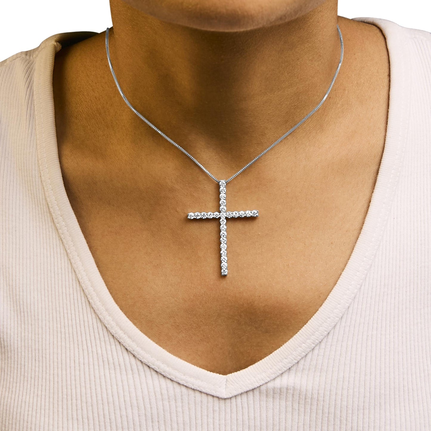 Close-up front view of a necklace on a model featuring a white metal cross pendant adorned with round white gemstones in prong settings.