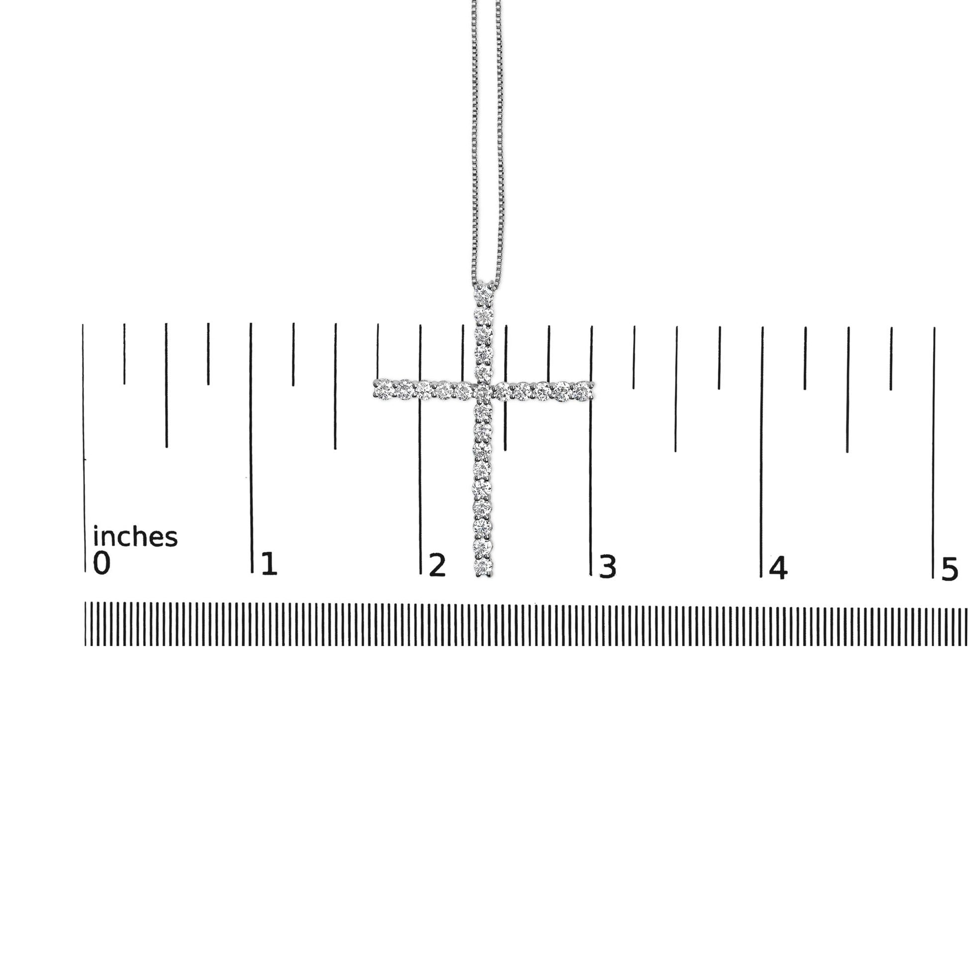 White metal necklace with cross pendant set with round white gemstones in prong settings, displayed on a ruler for size reference, shot from the front.