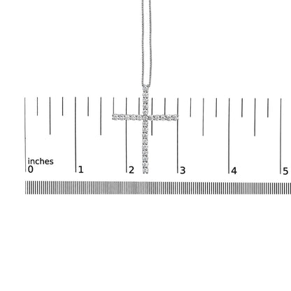White metal necklace with cross pendant set with round white gemstones in prong settings, displayed on a ruler for size reference, shot from the front.