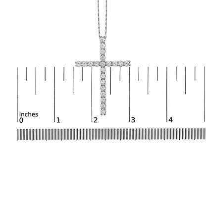 Close-up front view of a white metal cross necklace pendant with round white gemstones in prong settings, shown on a ruler for size reference.