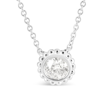 Close-up front view of a white metal necklace with a round bezel-set white gemstone pendant surrounded by a scalloped edge.