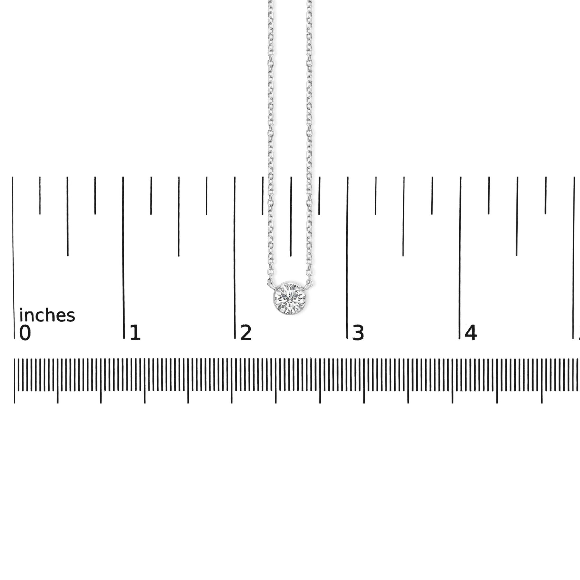 Top-down view of a white metal necklace with a single round white gemstone in bezel setting, placed on a ruler for size reference.