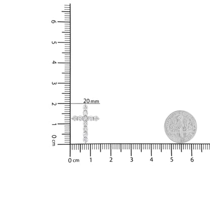 White metal cross-shaped necklace pendant with round white gemstones in prong setting, shown flat on a ruler for size reference with a coin nearby, top-down angle.