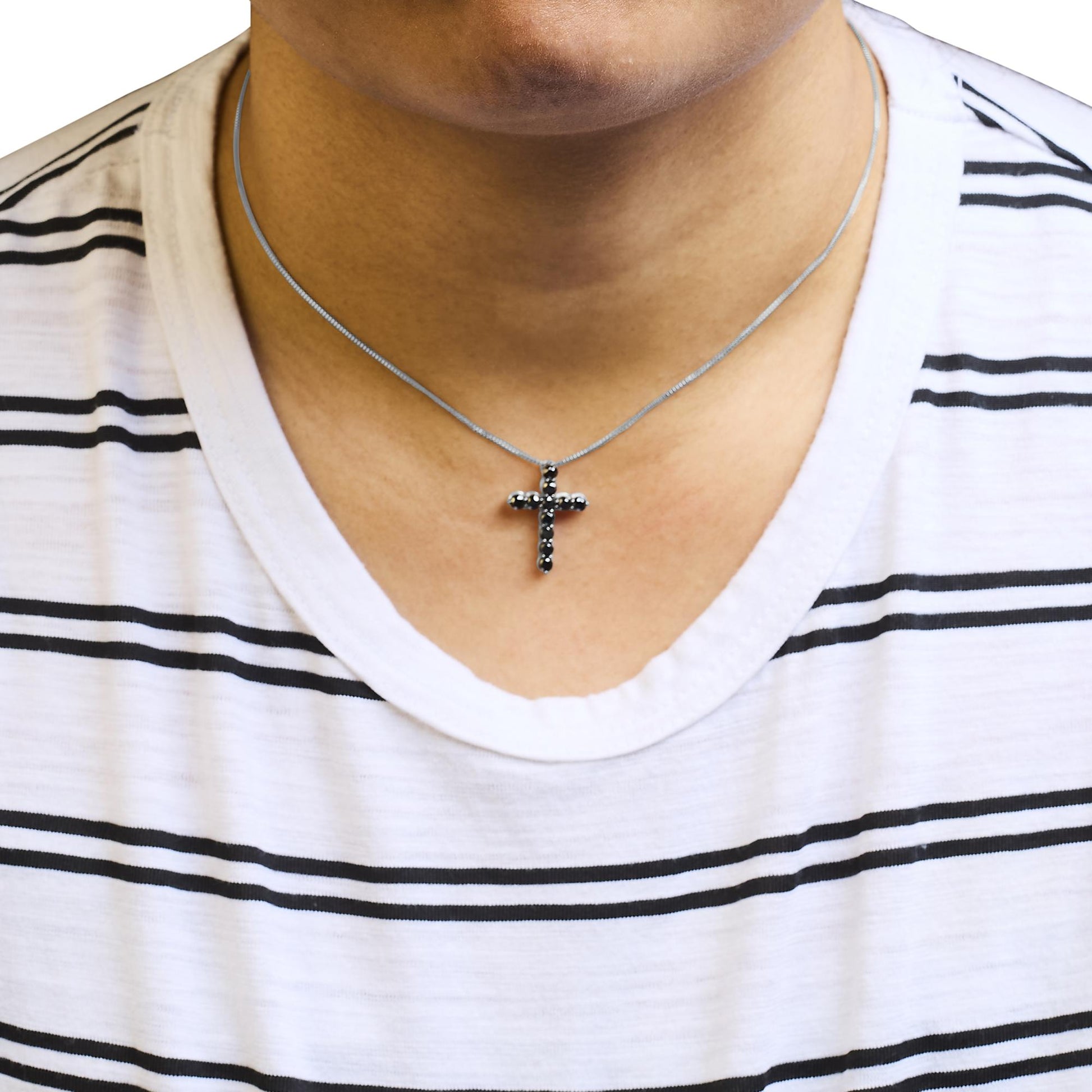 Close-up front view of a white metal necklace with a cross-shaped pendant set with round black gemstones, worn on a model.