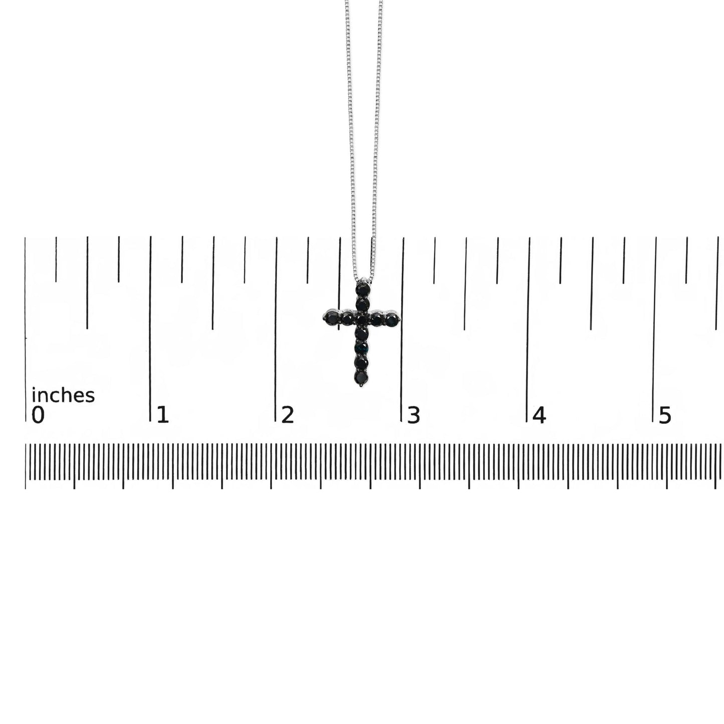 White metal necklace with a cross pendant set with round black gemstones in prong settings, shown hanging above a ruler for size reference, front-facing angle.