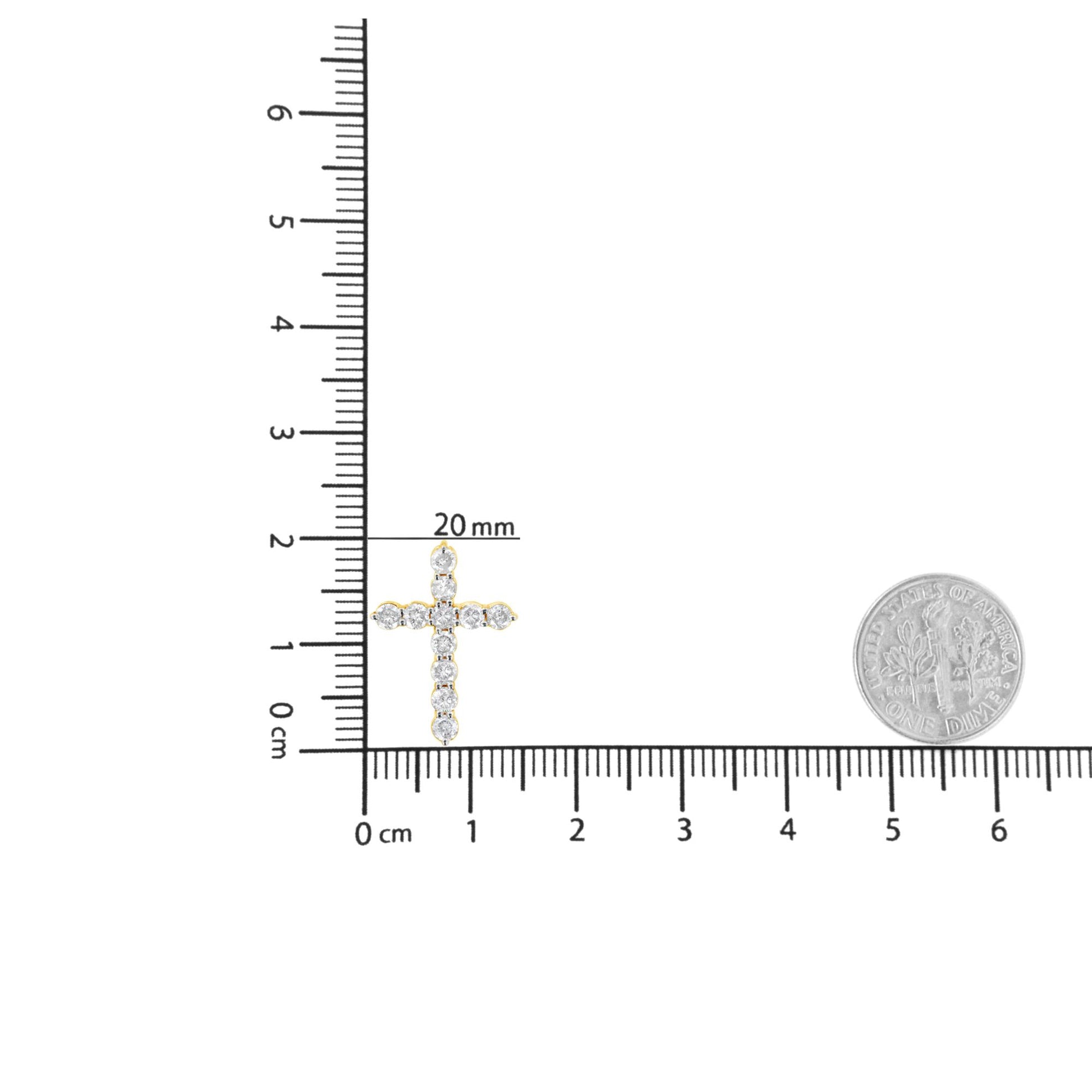 Close-up front view of a yellow metal cross-shaped necklace pendant with round white gemstones in prong settings, placed on a ruler for size reference.