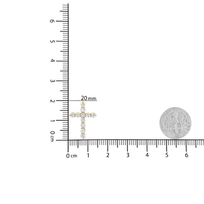 Close-up front view of a yellow metal cross-shaped necklace pendant with round white gemstones in prong settings, placed on a ruler for size reference.