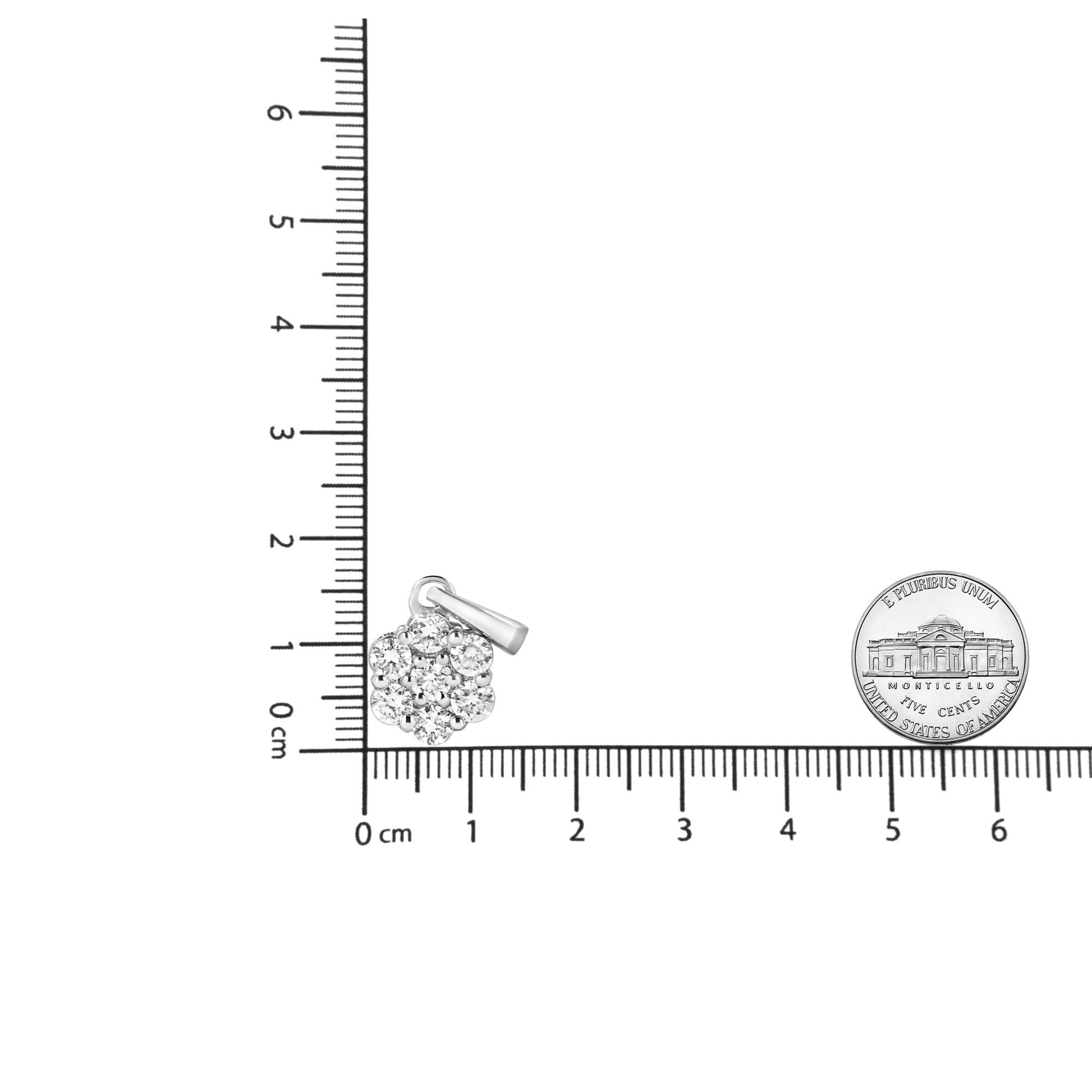 White metal necklace pendant with round prong-set white gemstones arranged in a cluster, shown on a ruler for size reference, front view.