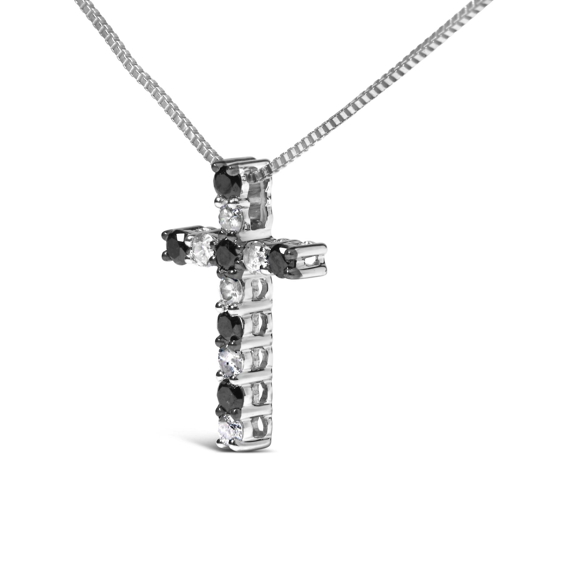 Close-up angled view of a white metal cross-shaped necklace pendant with alternating black and white round prong-set gemstones, hanging from a white metal box chain against a white background.