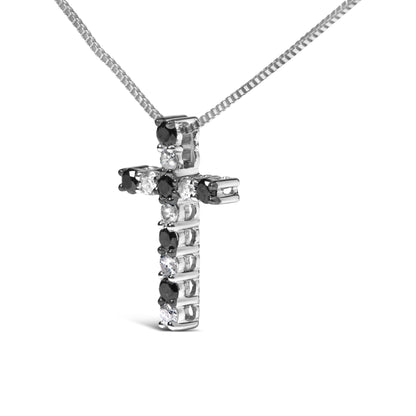 Close-up angled view of a white metal cross-shaped necklace pendant with alternating black and white round prong-set gemstones, hanging from a white metal box chain against a white background.