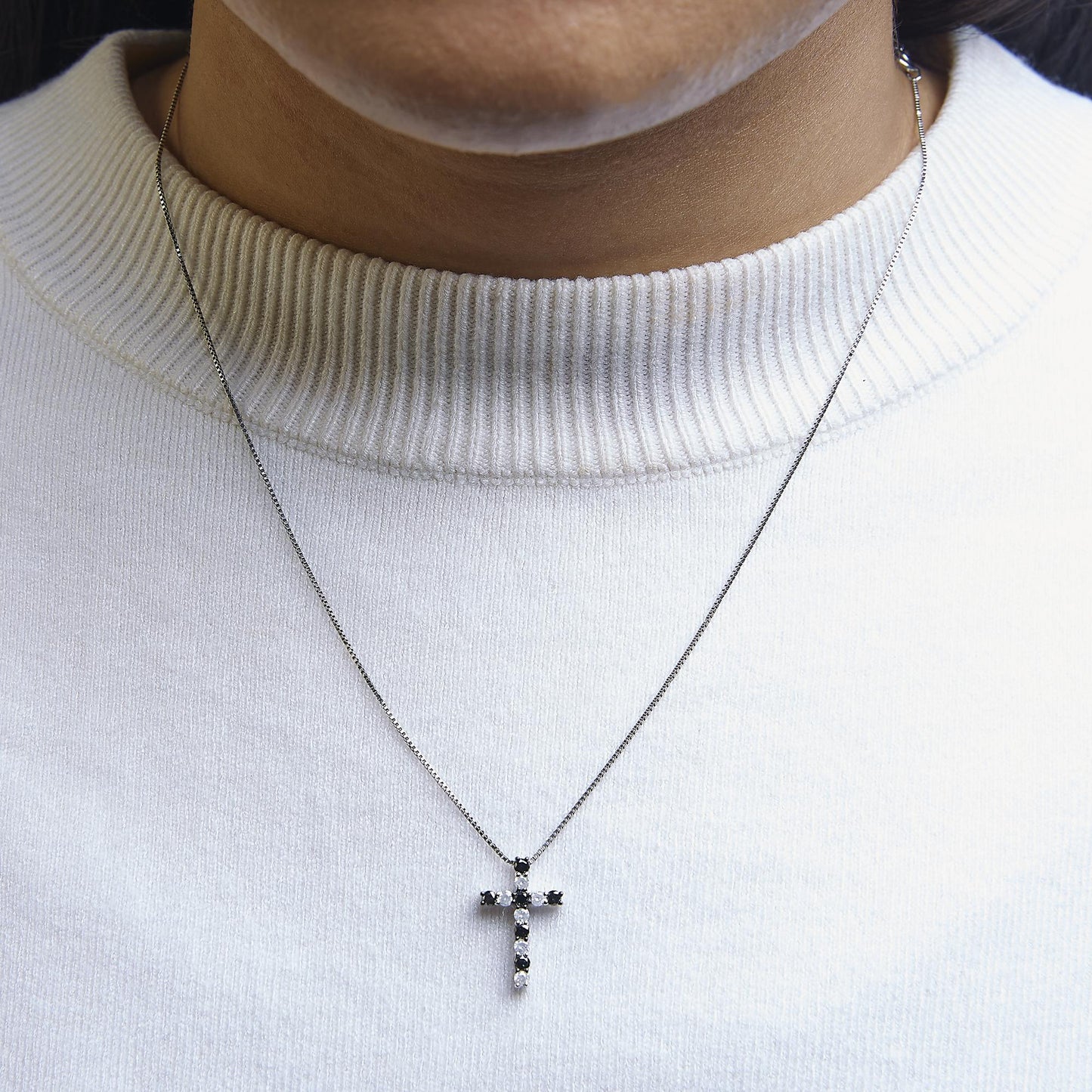 White metal necklace with a cross pendant featuring alternating black and white round gemstones in prong settings, shown worn on a model in a close-up front view.