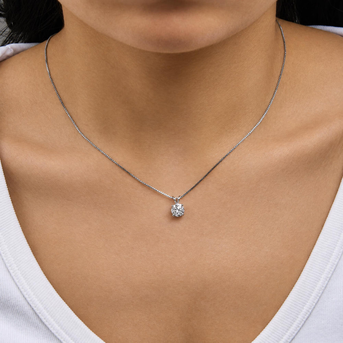 Close-up front view of a model wearing a white metal necklace with a round white gemstone pendant in a 4-prong setting.