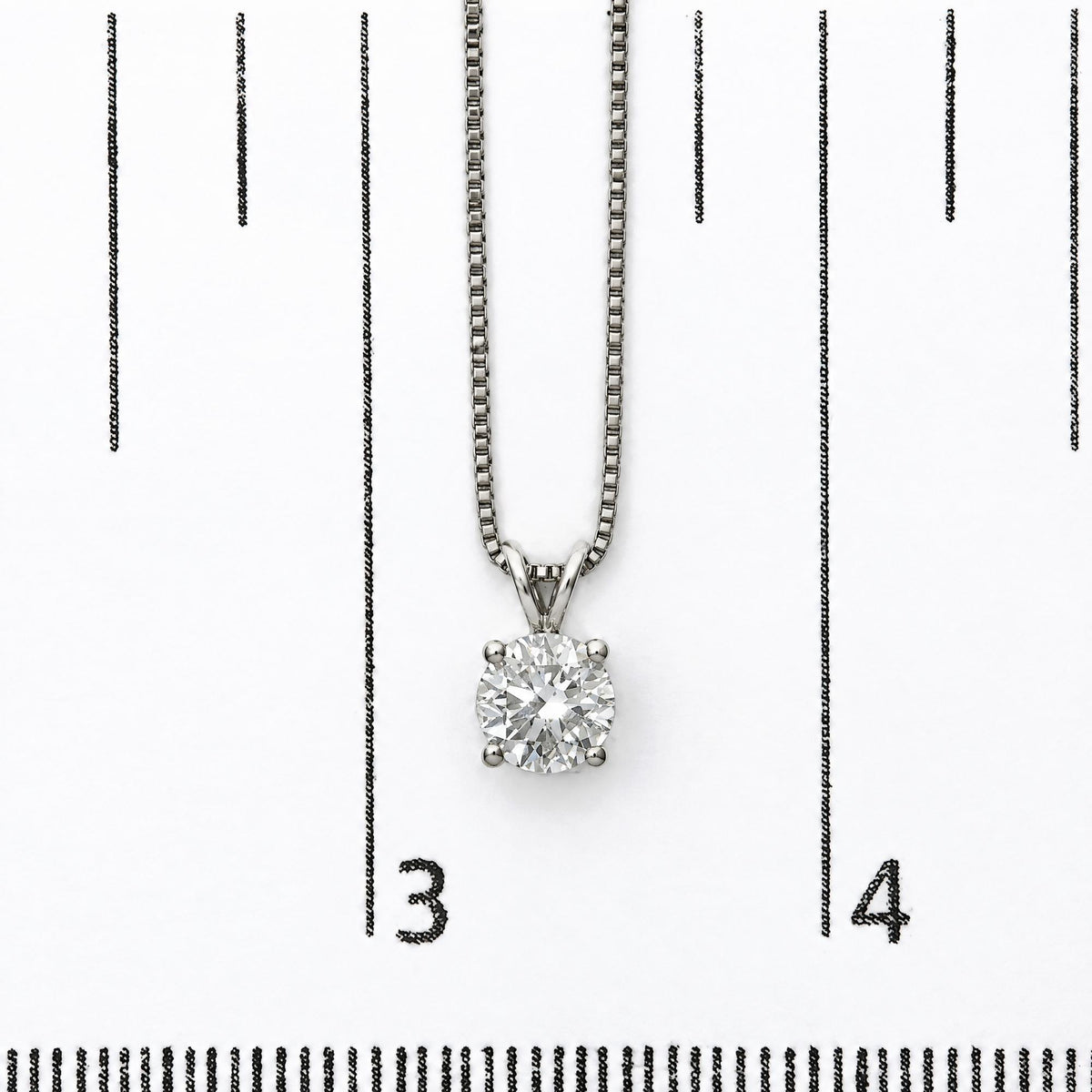 Close-up image of a white necklace with a round white gemstone in a 4-prong setting, shown on a scale.