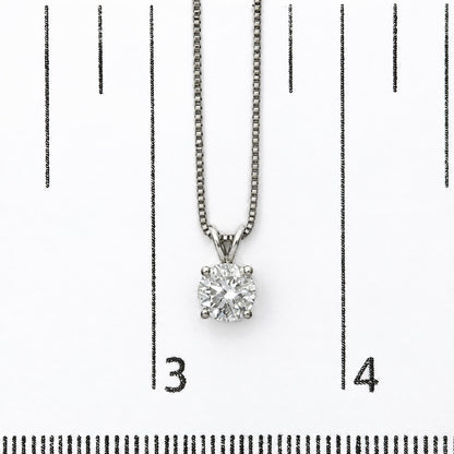 Close-up image of a white necklace with a round white gemstone in a 4-prong setting, shown on a scale.