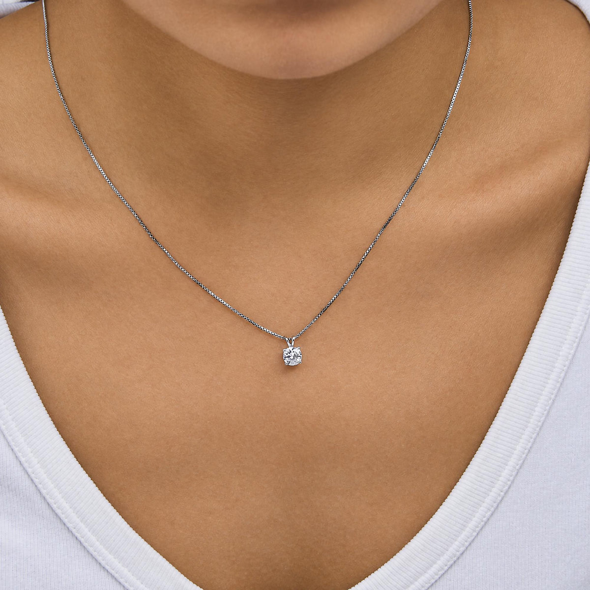 Close-up front view of a model wearing a white metal necklace with a single round white gemstone in a four-prong setting pendant.