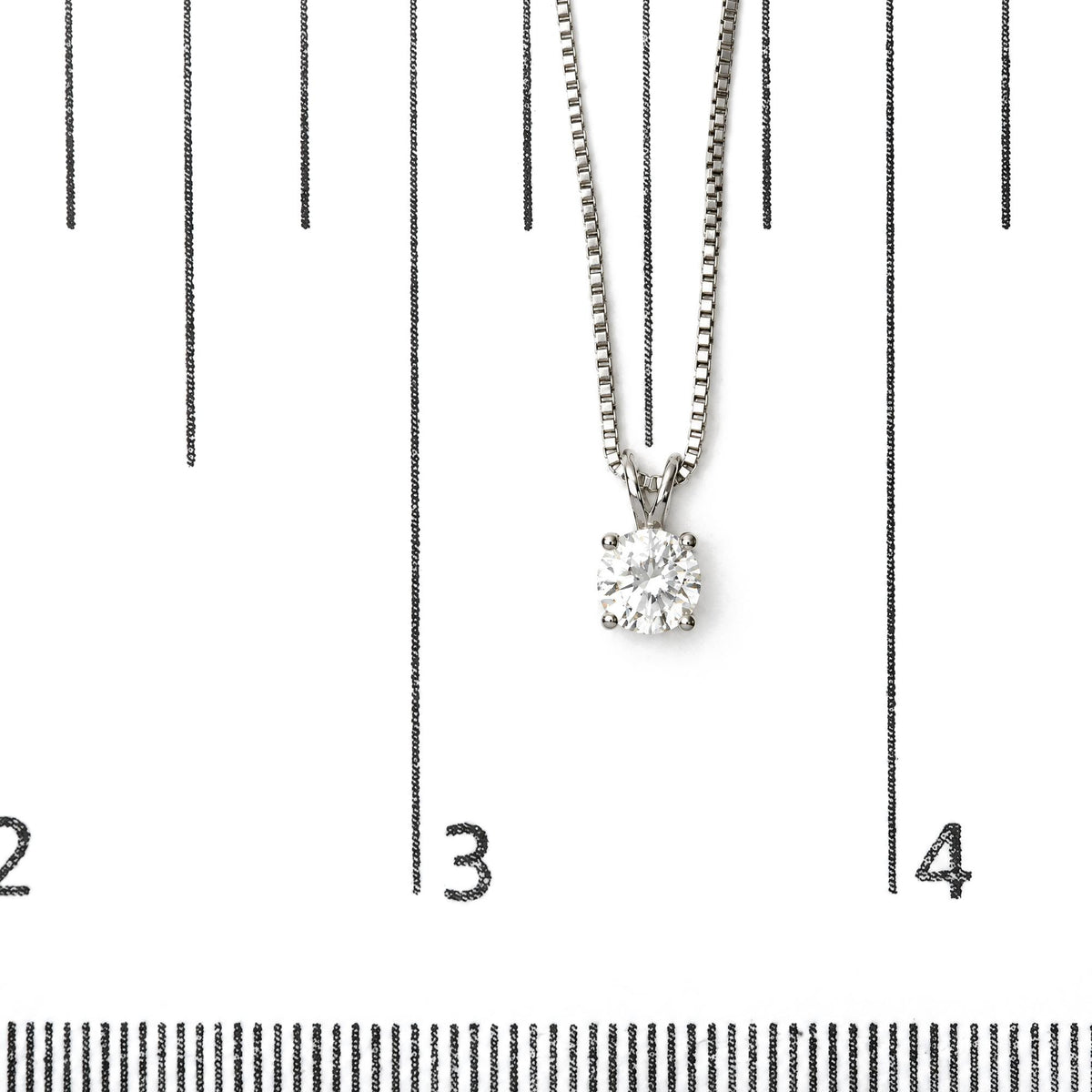 Close-up image of a white necklace with a round white gemstone in a four-prong setting, shown on a scale.